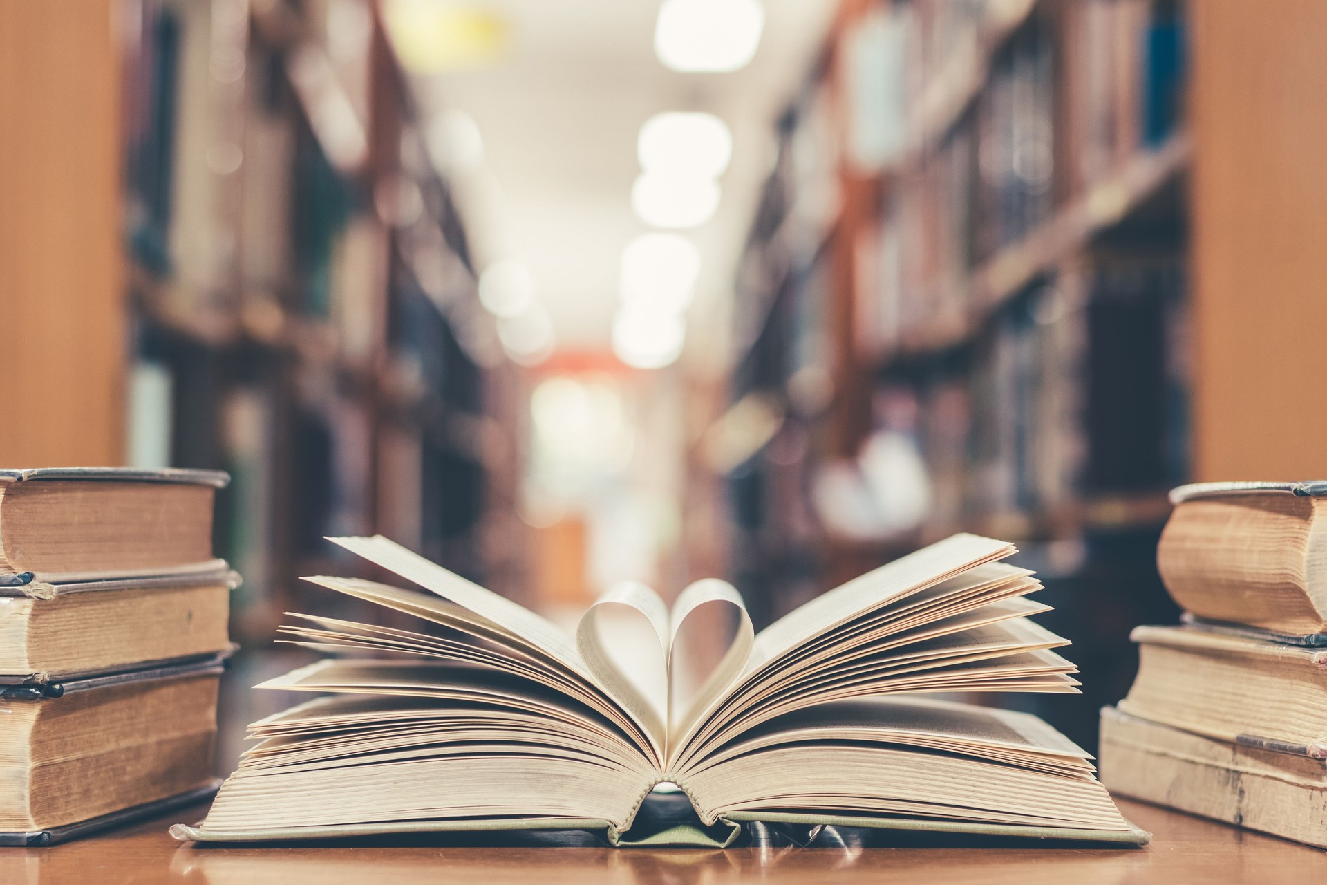 Love story book with open page of literature in heart shape and stack piles of textbooks on reading desk in library, school study room for national library lovers month  and education learning concept